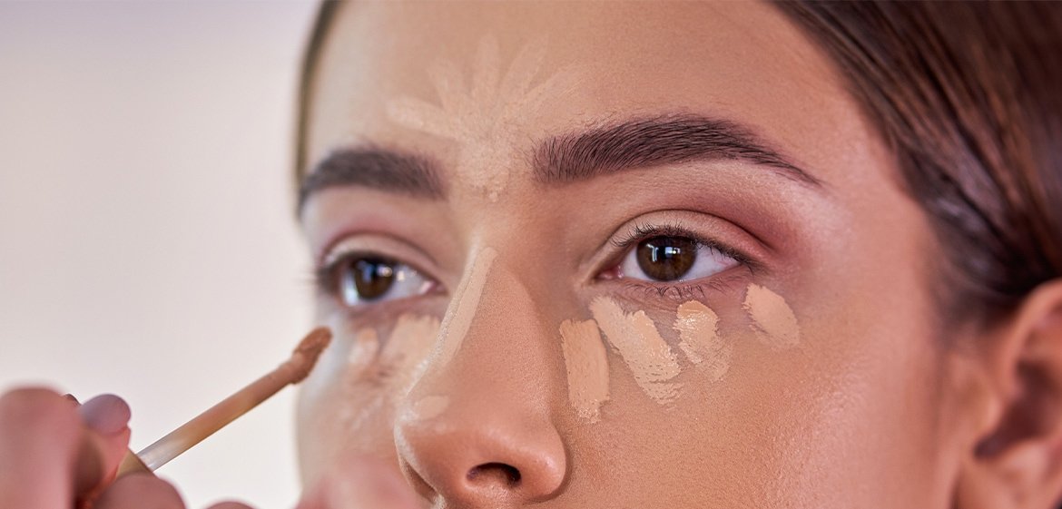 Junge Frau trägt Concealer unter ihren Augen, auf der Nase und Stirn auf.